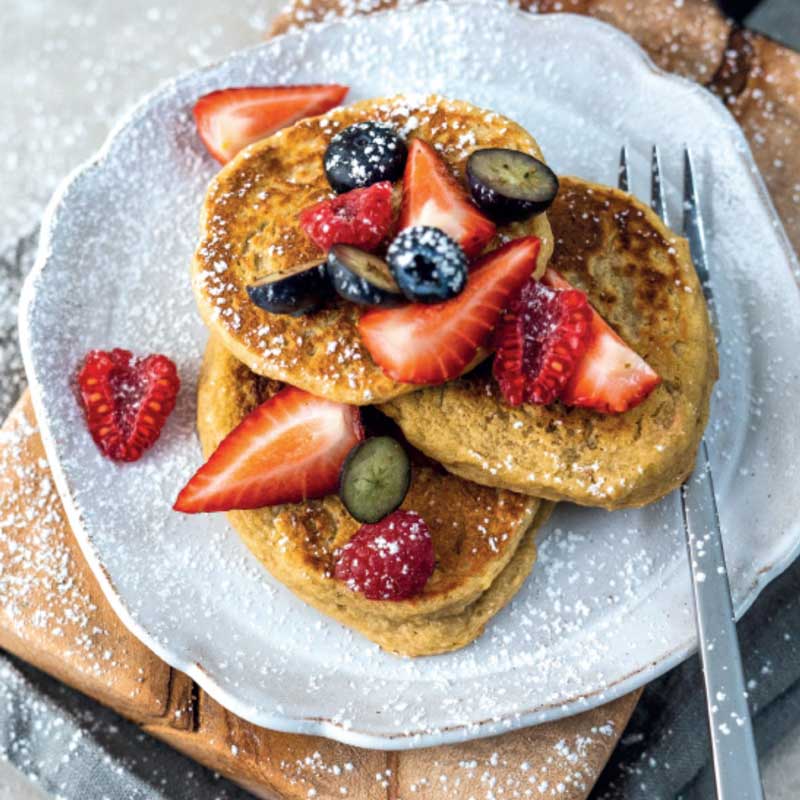 Pannkakor ligger på en tallrik, toppade med jordgubbar, hallon och blåbär. 